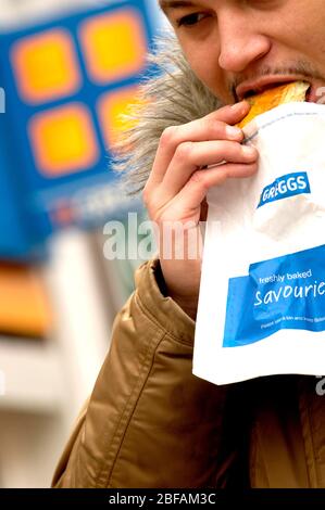 Ein Mann isst seine vor kurzem kaufen Greggs Essen. Stockfoto