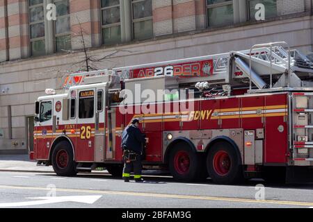 Ein Feuerwehrmann steht neben einem Feuerwehrwagen. Es liest Leiter 26 Harlem, Teil der Feuerwehr von New York oder FDNY Stockfoto