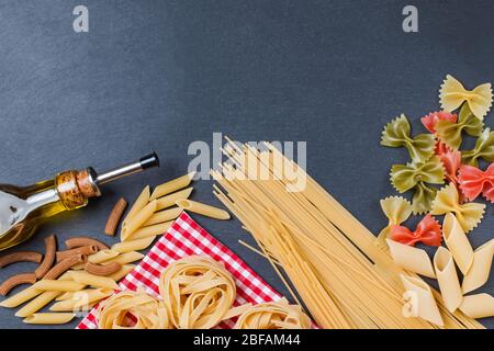 Verschiedene Arten von Pasta und eine Flasche Olivenöl auf schwarzem Schiefergrund Stockfoto