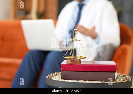 Bücher mit einer Skala von Gerechtigkeit auf dem Tisch und männliche Anwalt online zu Hause arbeiten Stockfoto