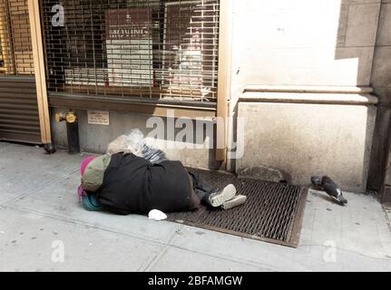 Obdachlose Person, die auf einem Gitter in der 57. Straße in Manhattan schläft. Tauben werden gesehen, die um die Person herumwandern, ein Symbol der Einkommensungleichheit Stockfoto