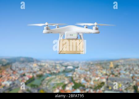 Technologische Sendung Innovation - Drohne schnelle Lieferung Konzept, Multicopter fliegen mit Karton über der Stadt Stockfoto