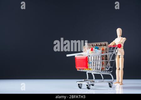 Holzpuppe hat gekauft und trägt Pillen und Medikamente in den Warenkorb. Bleibt auf grauem Hintergrund. Konzept der Gesundheit, Pillen und Medizin. Verschiedene Pille Stockfoto