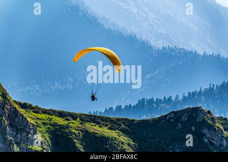 Gelber Gleitschirm über der Green Mountain Piste. Paragleiter fliegen über den Berghang am sonnigen Sommertag, Stockfoto