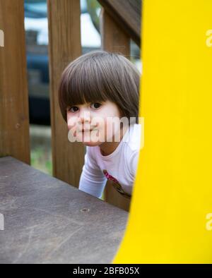 Verona, Italien - 29. März 2015: Kleines Mädchen peischt sich versteckt und sucht unter den Attraktionen eines Spielplatzes im Freien. Stockfoto