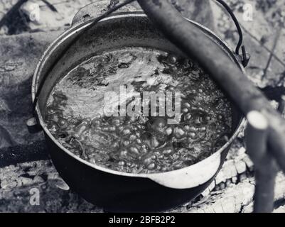 Borscht - Ukrainische traditionelle Suppe Kochen in alten rußigen Kessel am Lagerfeuer am Sommertag. Schwarzweiß getöntes Bild. Stockfoto