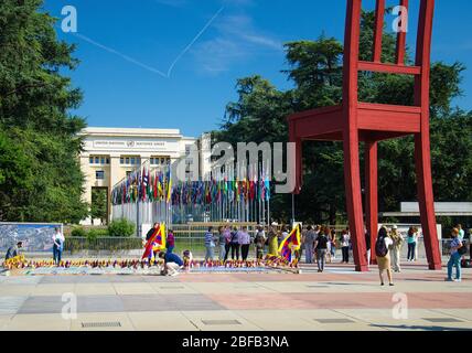 Genf, Schweiz - 14. September 2016: Gebrochener Stuhl auf dem Platz der Nationen und wandelende Menschen vor dem Palast der Vereinten Nationen Gebäude - Pea Stockfoto