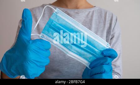 Hände in blauen Gummihandschuhen halten eine entfernte medizinische Maske mit Daumen nach oben. Sieg über Corona Virus. Ende der Epidemie. Stockfoto