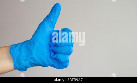 Linke Hand in blauem Handschuh mit Daumen nach oben. Negativer Raum. Platz für Text kopieren. Stockfoto