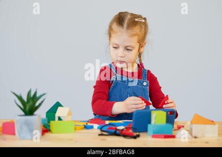 Online Fernstudium zu Hause während der Quarantäne. Ein intelligentes Kind mit Brille sammelt einen mehrfarbigen Konstruktor an einem Tisch im Klassenzimmer. Stockfoto