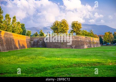 Defensive Backstein Stadtmauer, Gras grünen Rasen, Bäume und Toskana Hügel und Berge mit schönen bewölkten Abendhimmel Hintergrund, Lucca, Italien Stockfoto