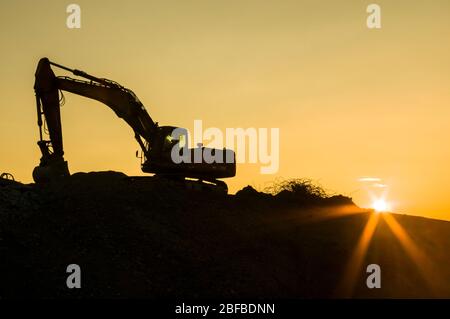 Baustellenidylle, Bagger auf Baustelle bei Sonnenuntergang mit Sonnenstein, Silhouette Stockfoto