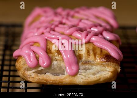 Strudel machen aus der Nähe frisch gebackenes Gebäck mit rosa Zuckerguss. Aus dem Ofen heiß schuppiger Dessertstrudel. Hausgemachte Backwaren. Stockfoto