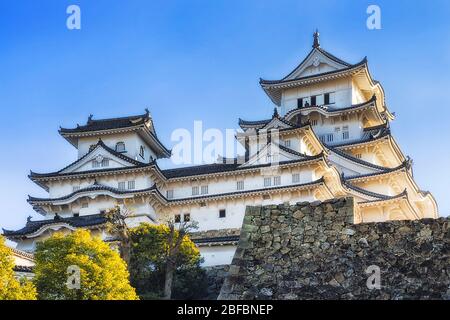 Weiße Mauern und Türme der historischen traditionellen japanischen Burg in Himeji über massiven Steinmauern gegen blauen Himmel. Stockfoto