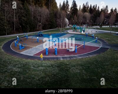 Ein einstehendes Kind, nicht identifizierbar, steht neben einem Spielplatz, der wegen der Covid 19 Pandemie mit Klebeband verschlossen wurde. Stockfoto