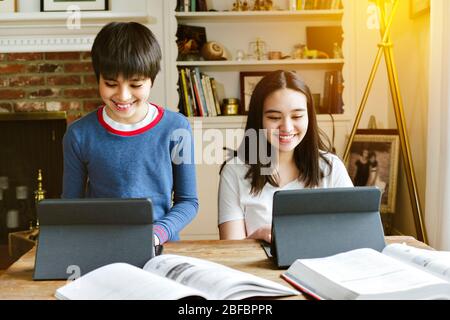 Geschwister machen ihre Schularbeit von zu Hause aus während der sozialen Distanz - Homeschool - Happy - Tablets Stockfoto