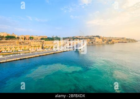 Sonnenaufgang am Grand Harbour von Valletta Malta mit Sonne, die die alte ummauerte Stadt trifft und einem kleinen Kreuzfahrtschiff auf der Mittelmeerinsel. Stockfoto