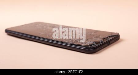 Gebrochenes Telefon auf einem beigefarbenen Hintergrund Nahaufnahme zerbrochenes Glas Display Smartphone. Stockfoto