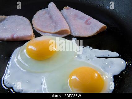 Zubereitung von überleichten Eiern und Schinken, auf einer Pfanne, als Teil des klassischen Frühstücks. Eier auf einem Topf-Konzept kochen. Stockfoto
