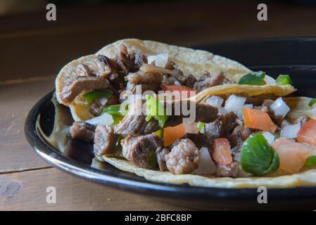 Mexikanische Carne asada Tacos oder gegrillte Rindfleisch Tacos mit Salsa Bandera oder Pico de gallo auf einem schwarzen Teller in einem Vintage-Holztisch, Taquitos als Teil von La Stockfoto