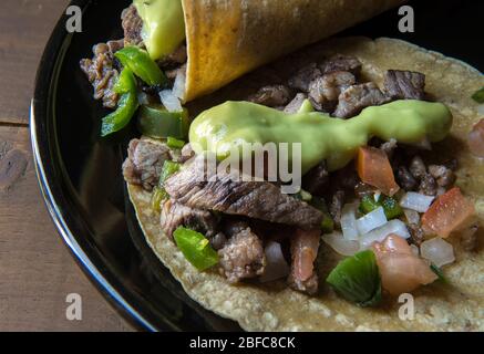 Mexikanische Rindfleisch Tacos oder mexikanische Taquitos mit Salsa und Avocado-Creme oder Guacamole auf einem schwarzen Teller auf einem Holztisch, Tacos mit Mais-Tortillas, Stockfoto