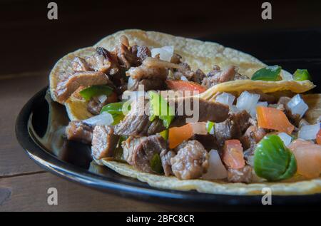 Mexikanische Carne asada Tacos oder gegrillte Rindfleisch Tacos mit Salsa Bandera oder Pico de gallo auf einem schwarzen Teller in einem Vintage-Holztisch, Taquitos als Teil von La Stockfoto