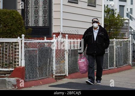 Chelsea, Massachusetts, USA. April 2020. Die COVID-19, Corona Virus, Situation in Chelsea, Massachusetts ist ein wichtiger Hotspot und die am härtesten getroffenen Stadt im Bundesstaat. Chelsea ist eine lateinamerikanische Einwandererbevölkerung mit 80% der Bevölkerung sind wichtige Arbeitskräfte, wie Lebensmittelarbeiter. Ein Mann geht die Straße hinunter in einer Maske. Kredit: Allison Dinner/ZUMA Wire/Alamy Live News Stockfoto