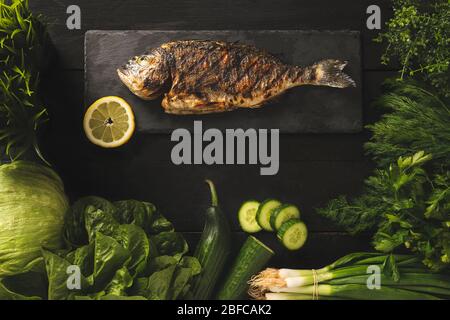 Gesundes Kochen. Brassen auf schwarzem Stein mit grünem Gemüse Stockfoto