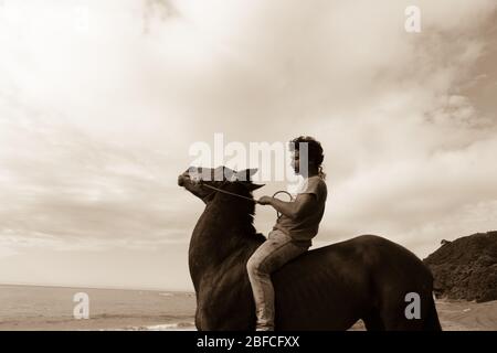 TE kaha Neuseeland im Januar 2013 ein junger Maori-Mann im grünen Hemd bareback reiten braunes Pferd am Strand entlang. Stockfoto