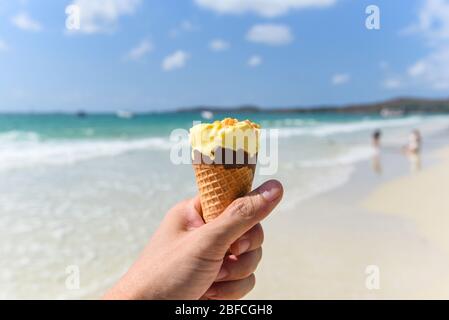 Schmelzen Eis am Strand im Sommer heißes Wetter Ozeanlandschaft Natur Outdoor-Urlaub , Gelbe Eis Mango mit Nüssen / Eis-Kegel in der Hand w Stockfoto