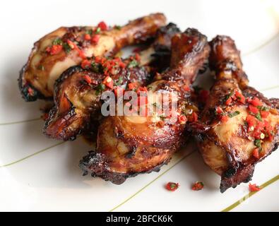 Gebackene Hähnchenschenkel. Serviert auf weißem Teller mit gehackten roten, kalten und minzfarbenen Blättern. Stockfoto