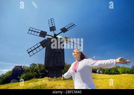 Schöne Ukrainische Mädchen tanzen in der Nähe von Holz- Wind Mill in weißen ethnischen Shirt auf nationaler Architektur Museum in Pirogowo. Kiew, Ukraine Stockfoto