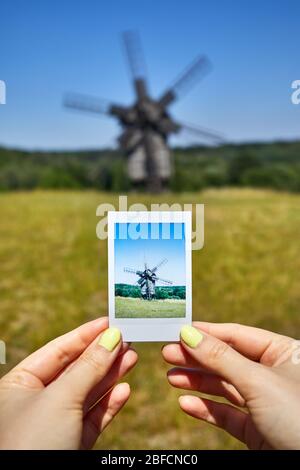 Frau mit Foto von Windmühle aus Holz auf der Wiese in der Architektur Museum in Pirogowo. Kiew, Ukraine Stockfoto