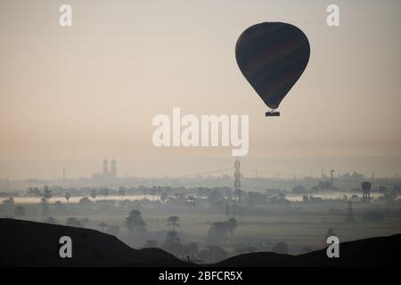 Heißluftballons, die über Luxor und der alten Stadt aufsteigen, wie vom Leichentempel der Hatschepsut am Westufer des Nils aus gesehen. Stockfoto