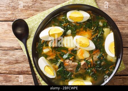 Eine heiße Suppe mit Fleisch, Spinat, Gemüse und Eiern in einer Schüssel auf dem Tisch. Horizontale Draufsicht von oben Stockfoto