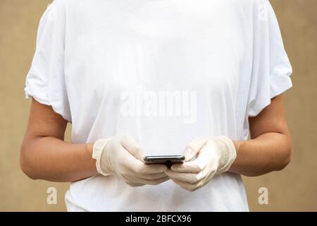 Frau, die Schutzhandschuhe trägt und mit ihrem Smartphone SMS schreibt oder chattet. Nahaufnahme der Hände, Tageslicht und Kopierfläche auf dem T-Shirt für Damen Stockfoto