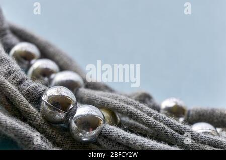 Weihnachten, Winter oder Schmuck Hintergrund. Handgefertigte graue Strickfäden mit verwitterten und zerkratzten Silberperlen auf blauem Hintergrund. Stockfoto