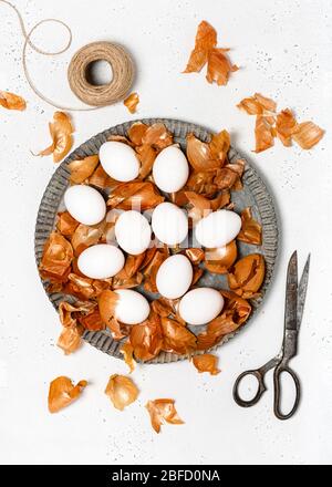 Rohe weiße Eier, Zwiebelschalen und Muster von frischen Kräutern. Prozess der Färbung von Eiern mit natürlichen Farben für Ostern. Selektiver Fokus. Stockfoto