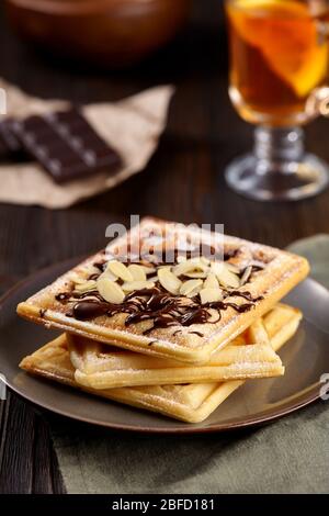 Wunderschönes Frühstück. Hausgemachte belgische Wiener Waffeln mit Schokolade und Erdbeeren, Tee auf dunklem Holzhintergrund dekoriert. Stockfoto