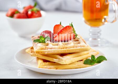 Wunderschönes Frühstück. Hausgemachte belgische Wiener Waffeln mit Erdbeeren, Tee auf einem hellen Hintergrund dekoriert. Stockfoto