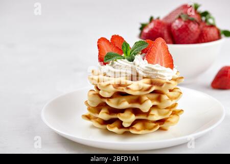 Wunderschönes Frühstück. Hausgemachte belgische Wiener Waffeln mit Erdbeeren, Tee auf einem hellen Hintergrund dekoriert. Stockfoto