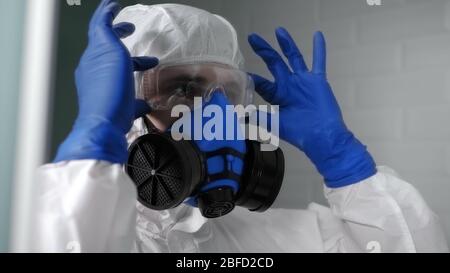 Nahaufnahme. Mann in Biogefährdung Schutzanzug Blick in den Spiegel Überprüfung Schutzbrille und Atemschutzmaske. Professionelle Aufnahme in 4K-Auflösung. 054. Stockfoto
