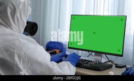 Mittlere Aufnahme. Ansicht zum Display. Ältere Arzt in Schutzanzug arbeiten am PC. Grüne Anzeige für Mock-Up. Professionelle Aufnahme in 4K-Auflösung. 05 Stockfoto