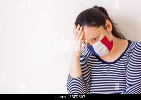 Das Mädchen in der medizinischen Maske, das wie die Flagge Frankreichs gemalt war, senkte nachdenklich ihren Kopf und legte ihre Hand auf den Kopf. Schaut zur Seite hinunter. Kopieren Stockfoto
