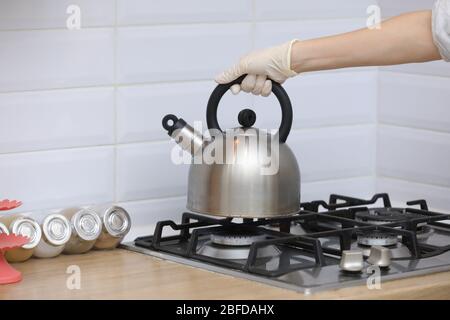 Frau stellt einen Wasserkocher auf die Küche in Handschuhen auf Gasherd. Herd Pfeifkessel in der Hand. Selektive Fokussierung. Stockfoto