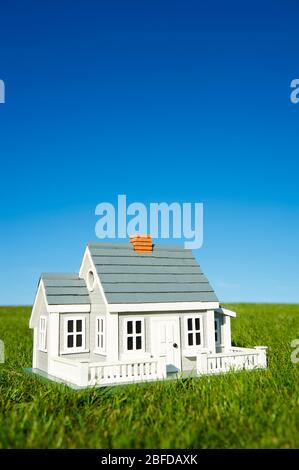 Miniaturhaus mit weißem Pickelzaun, der in einem grünen Rasen vor einem blauen Himmelshorizont steht Stockfoto