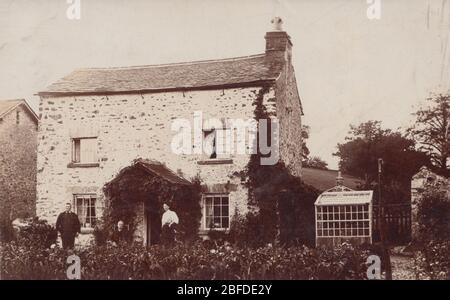 Britische Fotokarte aus dem frühen 20. Jahrhundert zeigt ein freistehendes ländliches Haus. Bewohner außerhalb des Grundstücks. Stockfoto