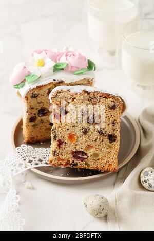 Scheibe Osterkuchen mit Rosinen und getrockneten Aprikosen. Hausgemachte Torte mit einem Glas Milch. Stück Kuchen mit Marzipan Blumendeko auf Teller. Holid Stockfoto