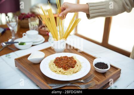 Köstliche Spaghetti Holztablett. Spaghetti Bolognese mit Hackfleisch, Zwiebel, gehackte Tomaten, Tomatenmark . Das Mädchen nimmt die Spaghetti. Schwarzer PEP Stockfoto