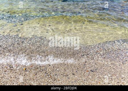 Meeresbrandung am Strand mit gelbem Sand oder Stein und kristallklarem Wasser in den Tropen. Nahaufnahme. Stockfoto